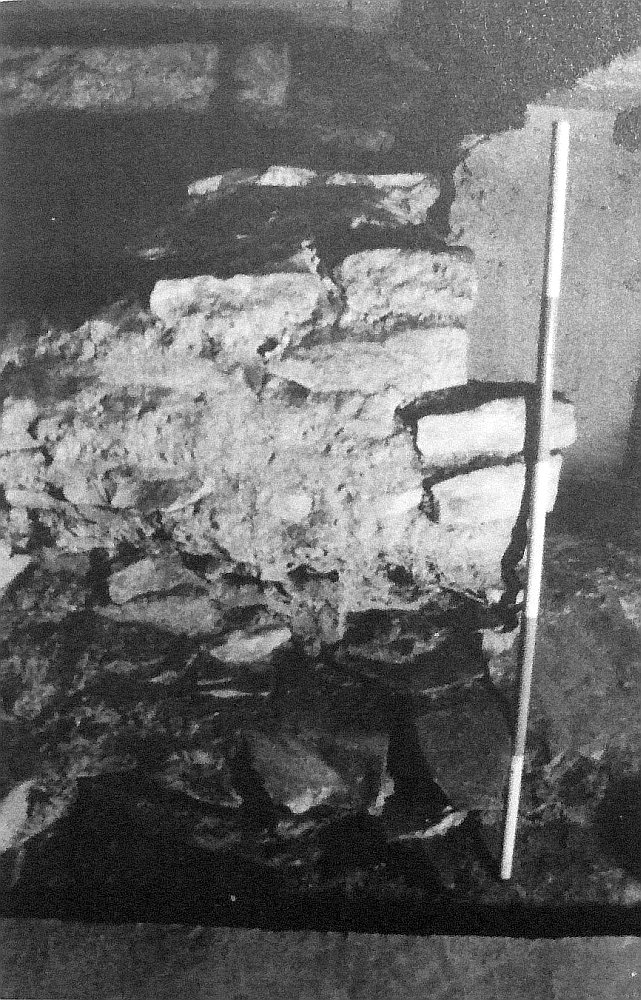 Pohled na severní zakončení vnitřního prstence zdiva od východu. Dole patrný nepravidelný, patrně ubouraný líc (tj. zdivo by pokračovalo směrem dopředu – k fotografovi, fáze 2A), na něm blok zdiva, oddělený ústupkem (patrným vpravo), zbytek oltáře 12 apoštolů (fáze 3B). Pohled od východu. Převzato z Castrum Pragense 3 (2000). Ve skutečnosti žádné stopy po odbourání líce zdiva vnitřního prstence nevidíme. Pouze směrem do vnitřku rotundy byl vytvořen líc z kvádříkového zdiva (opírá se o něj z boku trasírka). Ustupující dvě řady kvádříků nahoře jsou tzv. základem oltáře 12 apoštolů, rovněž přizděného k vnějšímu prstenci. Zhruba ve středu obrazu je viditelný začátek stavební spáry pokračující mírně šikmo doleva nahoru. Pod ní je rozrušené zdivo po odbourání zdi lodi první rotundy, která probíhala směrem k divákovi. 4_46a