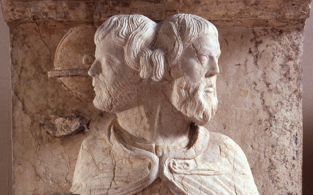 Bůh Janus s levou mladistvou tváří a pravou postarší z bývalé výzdoby portálu katedrály ve Ferraře v Itálii. Vznik mezi roky 1230–1250. Vyobrazení převzato z https://artsandculture.google.com/asset/giano-bifronte-gennaio/NwGhsXDfbHe8Xw (výřez). Janus-rom._kat._Ferrara